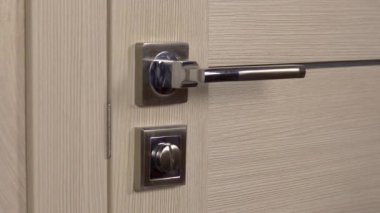 A young woman enters a dark room. The woman lowers the door handle and opens it closeup. The room is in the dark.