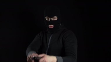 Kar maskeli bir adam elinde silahla ayakta duruyor. Bir haydut silahını kameraya doğrultuyor. Siyah bir arkaplanda.