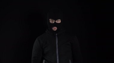 Kar maskeli bir adam elinde çiçeklerle dikiliyor. Haydut elinde bir buket pembe çiçek tutuyor ve siyah bir arka planda gülümsüyor..