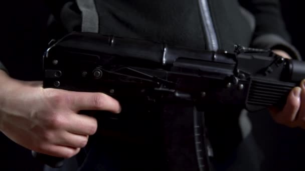 Un bandit tient un fusil à la main sur un fond noir. Gros plan panoramique de gauche à droite. — Video
