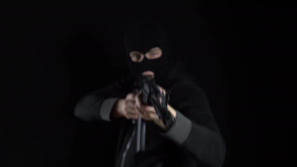 Человек в балаклавской маске стоит с автоматом АК-47. Бандит целится в пулемет и стреляет в камеру. На черном фоне . — стоковое видео