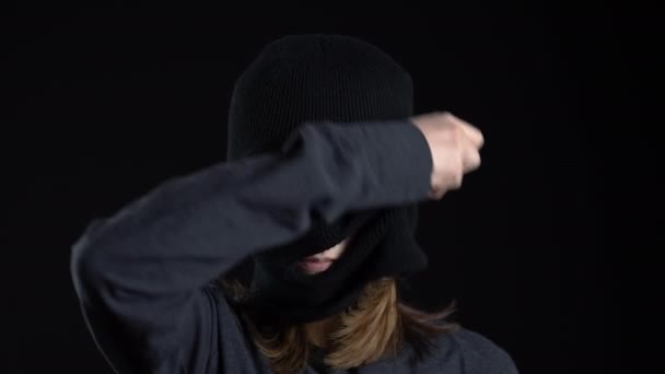 Молода жінка знімає маску балаклави. Бандит на чорному тлі крупним планом . — стокове відео