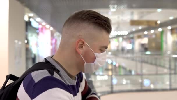 Een jongeman met een medisch masker op de tweede verdieping in een winkelcentrum. De man hoest. De gemaskerde man beschermt zichzelf tegen de epidemie van het Chinese virus "2019-nkov" — Stockvideo