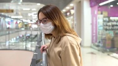 Young woman in a medical mask on the second floor in a shopping center. A woman looks down from behind the railing. The masked woman protects herself from the epidemic of the Chinese virus 