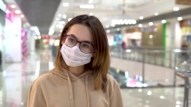 Молодая женщина в медицинской маске гуляет в торговом центре. Женщина в маске защищает себя от эпидемии китайского вируса "2019-nKoV ". — стоковое видео
