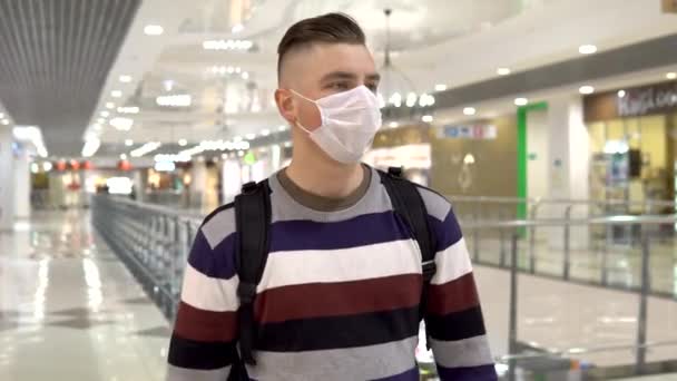 Um jovem com uma máscara médica caminha num centro comercial. O homem está a tossir. O homem mascarado protege-se da epidemia do vírus chinês "2019-nKoV " — Vídeo de Stock