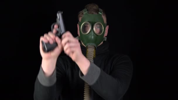 A man in a gas mask stands with a gun. The bandit is loading the gun. On a black background. — Stockvideo