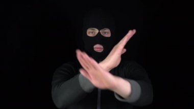 Kar maskesi takmış bir adam elleriyle negatif bir işaret gösterir. Eşkıya siyah bir arka planda kollarını kavuşturdu..