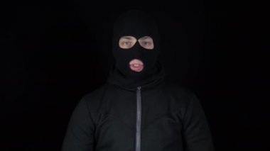 Kar maskeli bir adam elleriyle onay işaretini göstermiş. Eşkıya ellerini kaldırdı ve siyah arka planda baş parmaklarını gösterdi..