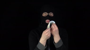 Kar maskeli bir adam bir tomar dolarla ayakta duruyor. Haydut parayı karıştırıyor ve seviniyor. Siyah bir arkaplanda.