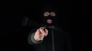 Kar maskeli bir adam kameraya kelebek bıçağı doğrultuyor. Eşkıya, siyah arka planda bıçak büküyor..