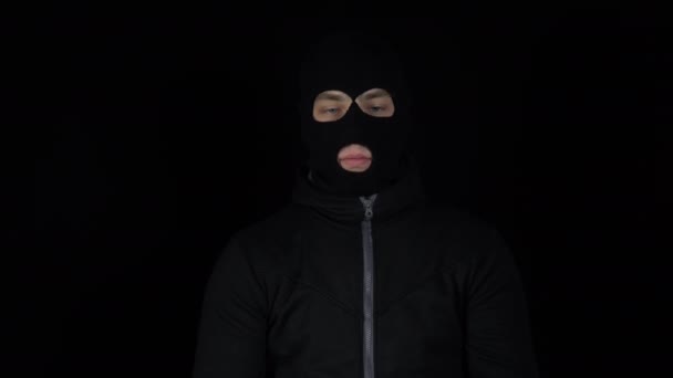 Un homme avec un masque de cagoule est debout avec un paquet d'euros. Le voyou feuillette l'argent et se réjouit. Sur fond noir. — Video