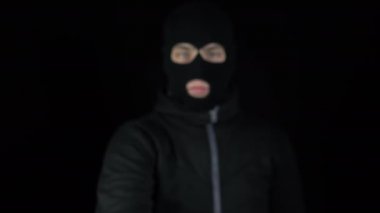 Kar maskeli bir adam biber gazıyla ayakta duruyor. Bir haydut kameraya biber gazı sıkıyor. Siyah bir arkaplanda.