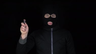 Kar maskeli bir adam biber gazıyla ayakta duruyor. Biber gazı savunma silahı. Siyah bir arkaplanda.
