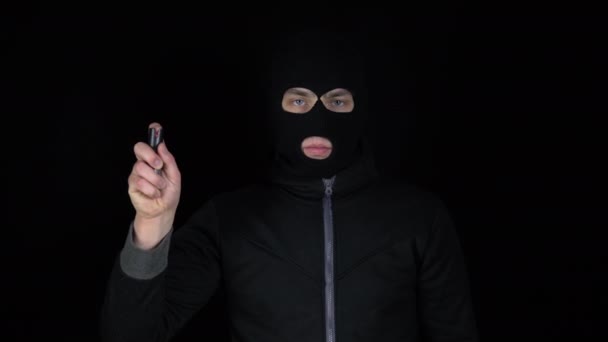 En man i en balaclava mask står med en pepparspray. Pepparsprej självförsvar vapen. På en svart bakgrund. — Stockvideo