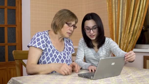 Дочь учит мать пользоваться ноутбуком. Молодая женщина показала, как открыть ноутбук своей старой матери. Женщина удивлена. Семья сидит в комфортабельной комнате . — стоковое видео