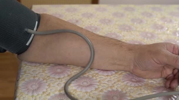 A person uses a device to measure cardiovascular pressure. The man put the blood pressure monitor on his hand and measures the pressure close-up. — 图库视频影像