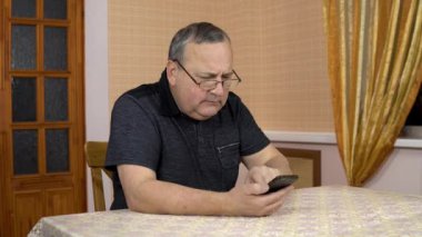 A man uses a telephone for the first time. The old man hardly dialed the number and started talking on the phone. A man in a comfortable room.