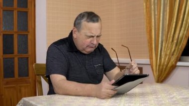 A man uses a tablet for the first time. An old man is having difficulty using a tablet. A man in a comfortable room.