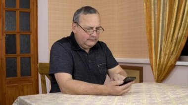 A man uses a phone with a serious face. The old man dialed the number and started talking on the phone. A man in a comfortable room.