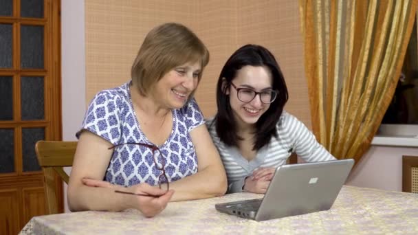 La fille et sa mère communiquent avec des amis par liaison vidéo via un ordinateur portable. Une jeune femme et une vieille mère communiquent et agitent leurs mains, regardant dans un ordinateur portable. La famille est assise — Video