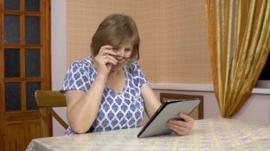 A woman uses a tablet for the first time. The old woman does not understand how to use the tablet, pokes her finger, and then puts it off. A woman in a comfortable room.