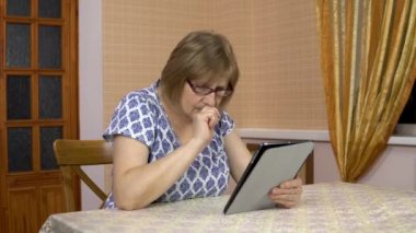 A woman is using a tablet for the first time. An old woman is having difficulty using a tablet. Woman in a cozy room.