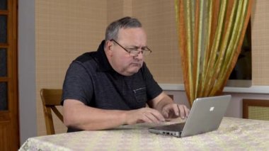 Man is using a laptop for the first time. The old man hardly uses a laptop hard presses the buttons. Man in a comfortable room.
