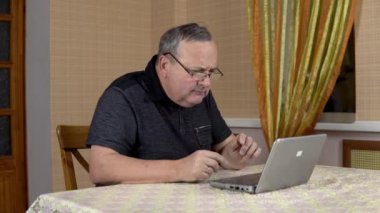 Man is using a laptop for the first time. The old man hardly uses a laptop hard presses the buttons. Man in a comfortable room.