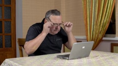 Man is using a laptop for the first time. The old man hardly uses a laptop hard presses the buttons. Man in a comfortable room.