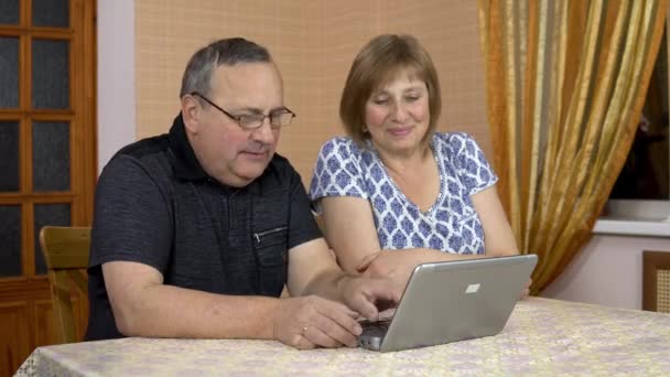 Un hombre y una mujer se comunican con amigos a través de la comunicación por vídeo a través de un ordenador portátil. Una joven se acercó a sus padres y también comenzó a comunicarse. La familia está sentada en una habitación cómoda . — Vídeos de Stock