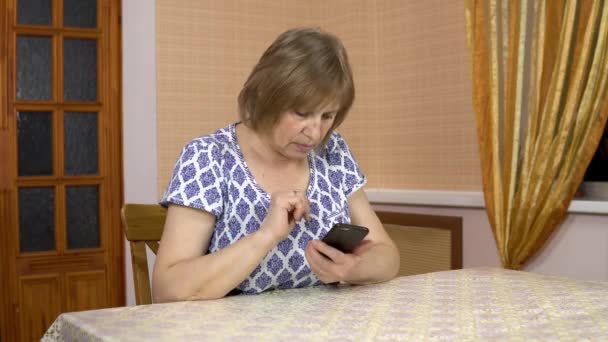 Una donna usa un telefono per la prima volta. La donna anziana non capisce come usare il telefono, punta il dito e poi lo lancia. Donna in una stanza accogliente . — Video Stock