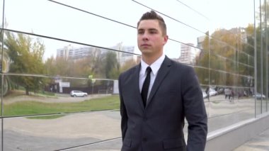A young businessman in a suit walks along a business center. A serious man. Mirrored Business Center. Slow motion
