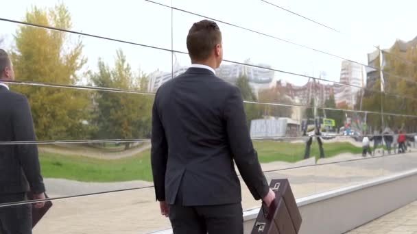 A young businessman in a suit walks along a business center. A serious man carries a case. Mirrored business center. View from the back. Slow motion — Stock video