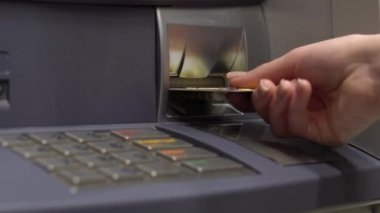 A young woman inserts a bank card into an ATM. ATM for cash withdrawal and deposit. Womans hand close-up.