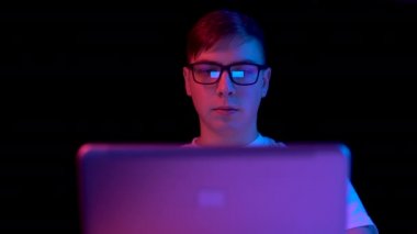 Young man with a laptop. A man uses a laptop. Blue and red light falls on a man on a black background.