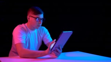 Young man with a tablet. A man is using a tablet. Blue and red light falls on a man on a black background.