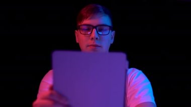 Young man with a tablet. A man is using a tablet. Blue and red light falls on a man on a black background.