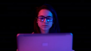 Young woman with a laptop. A woman is using a laptop. Blue and red light falls on a woman on a black background.