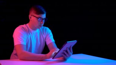 Young man with a tablet. A man is using a tablet. Blue and red light falls on a man on a black background.