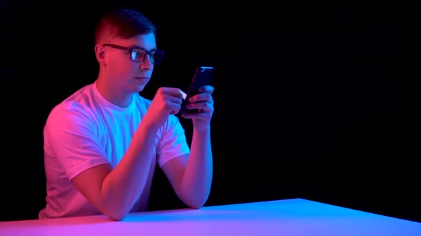 Young man with a smartphone. A man is using a telephone. Blue and red light falls on a man on a black background. — Stockvideo