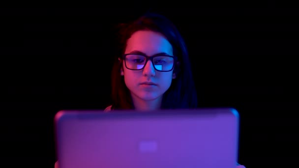 Young woman with a laptop. A woman is using a laptop. Blue and red light falls on a woman on a black background. — Wideo stockowe