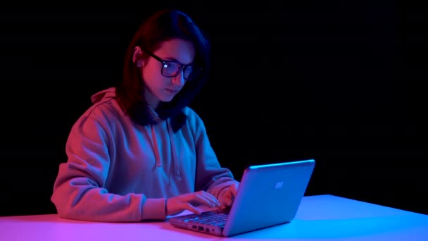 Young woman with a laptop. A woman is using a laptop. Blue and red light falls on a woman on a black background. — Wideo stockowe
