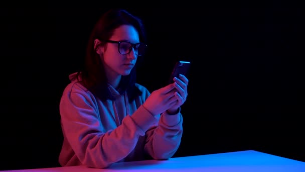 Young woman with a phone. A woman is talking on the phone. Blue and red light falls on a woman on a black background. — Stok video