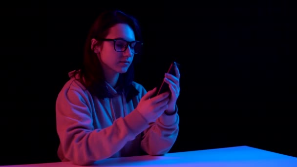 Young woman with a phone. A woman is talking on the phone. Blue and red light falls on a woman on a black background. — Wideo stockowe