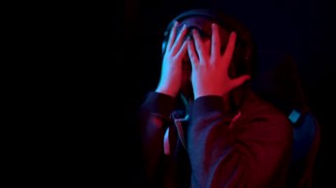 A young man sits at a computer and screams. The man in the hood looks at the monitor and curses with anger. The camera zooms out from behind the monitor