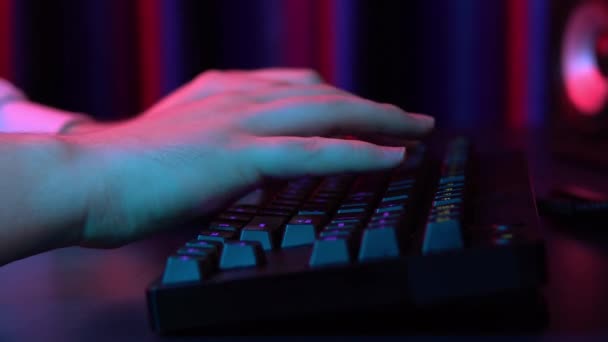 A young man is typing on a computer keyboard. Hands close up. Blue and red light falls on the hands. — Stockvideo