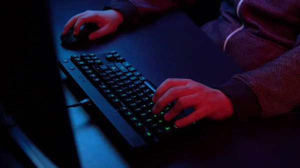 Un jeune homme joue à l'ordinateur. Mains travaillant sur le gros plan du clavier. La lumière bleue et rouge tombe sur les mains . — Photo