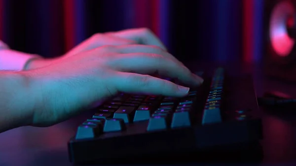 Un jeune homme tape sur un clavier d'ordinateur. Les mains en l'air. La lumière bleue et rouge tombe sur les mains . — Photo