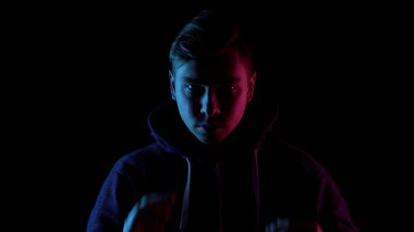 Saldırgan karanlıkta dikiliyor. Mavi ve kırmızı ışık siyah arka plandaki kişinin üzerine düşüyor..